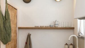 A compact kitchen with a wooden shelf, a sink, and two wall-mounted lights. - Aelios Cycladic house (Ormos Panormou)