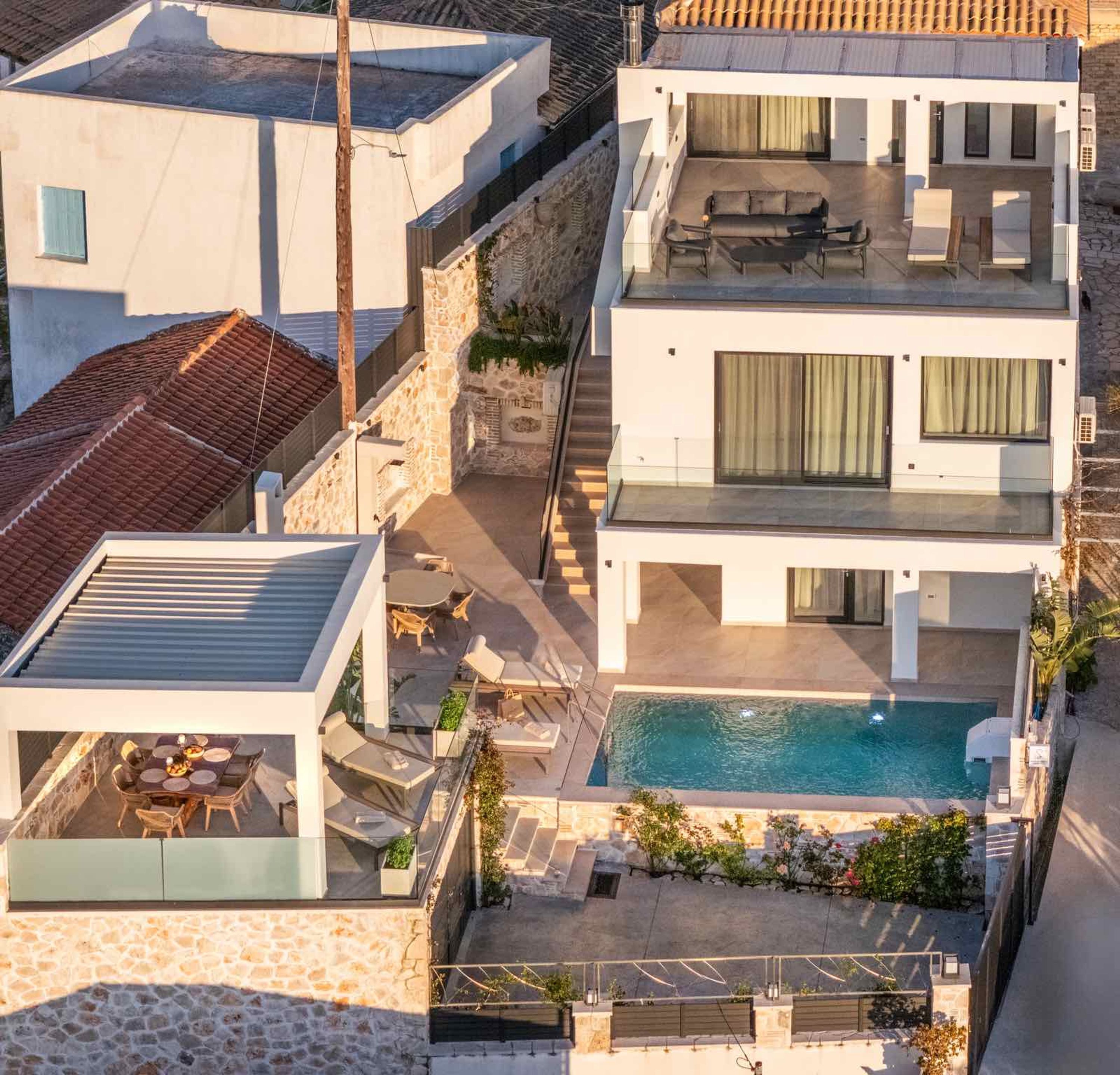 Une maison moderne à plusieurs étages, dotée d’une terrasse sur le toit, d’une piscine et d’un espace patio.