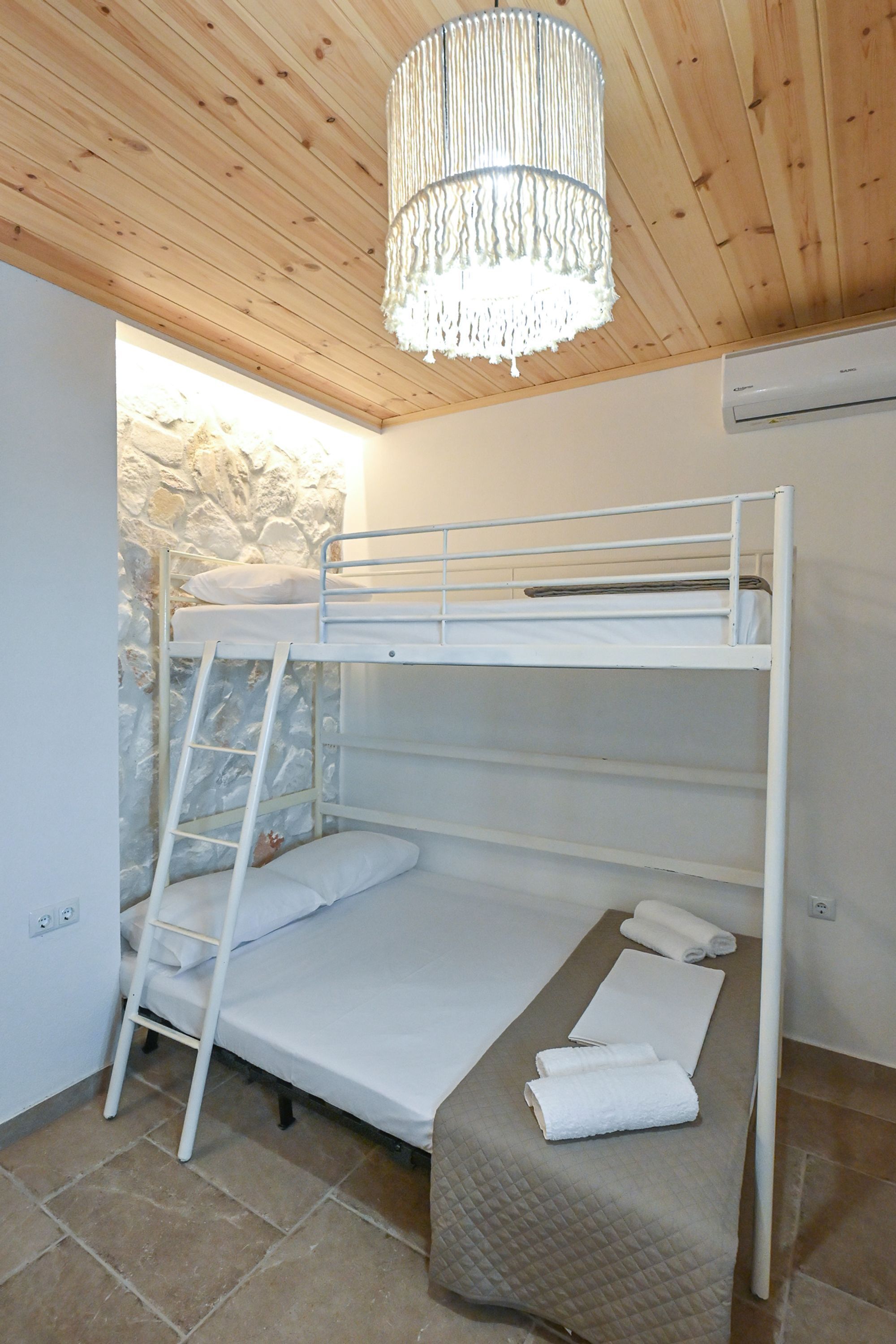 A bunk bed room with a stone wall, a wooden ceiling, and a hanging light fixture.