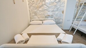 Un letto rifatto con cuscini e asciugamani arrotolati, una parete in pietra e una scala bianca.