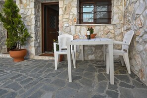 A stone building with a table and chairs outside, a potted plant, and a door. - Studio with Garden View (Fourka)
