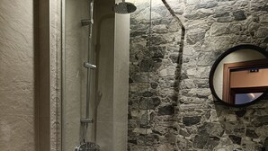 Un bagno con cabina doccia in vetro, un lavandino bianco e una parete in pietra.