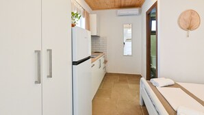Ett kompakt kök med kylskåp, spis och diskho, ett litet fönster och en säng med vita sängkläder.