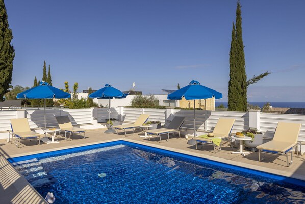 Ein Pool auf dem Dach mit blauen Sonnenschirmen, Liegestühlen und freiem Blick auf das Meer.