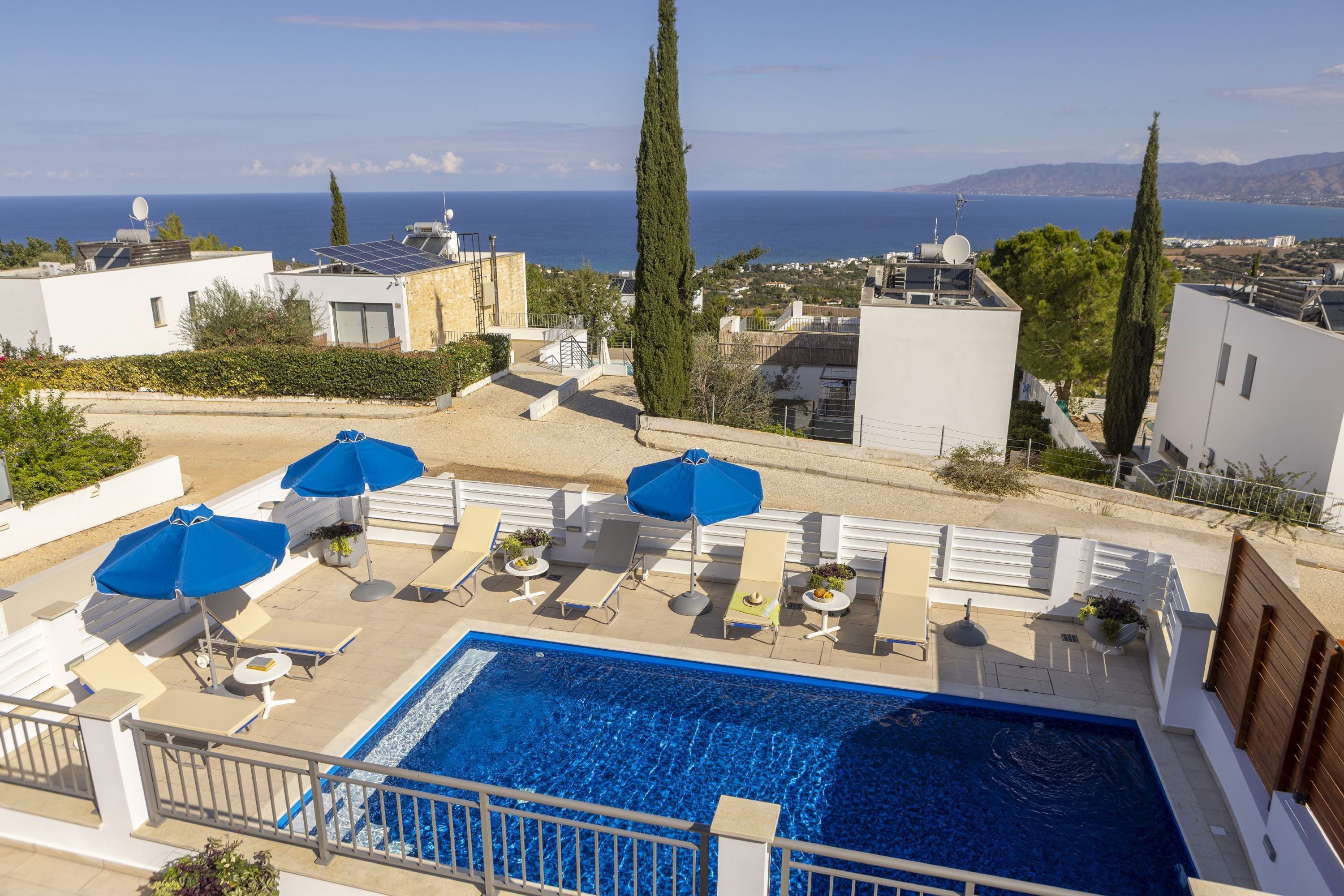 A rooftop pool with blue umbrellas, lounge chairs, and a view of the sea and buildings.