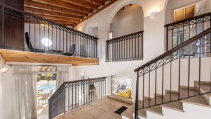 Ein mehrgeschossiges Interieur mit Treppe, Holzbalken und Blick auf einen Pool.