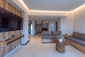 A modern living room with a flat-screen TV, a wooden accent wall, a grey sofa, and a coffee table with flowers. - Villa Dorothea in Georgioupoli (Georgioupoli)