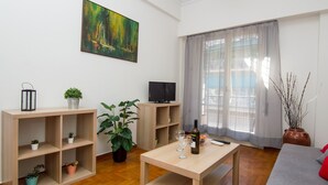 Ein modernes Wohnzimmer mit Holzboden, einem Fernseher, einem Tisch mit Flasche und Glas sowie Topfpflanzen.
