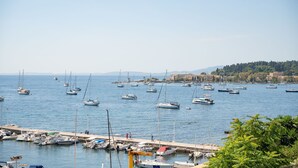 Ein Yachthafen mit zahlreichen Booten, eine Pier mit Spaziergängern und eine Kulisse aus Hügeln und Gebäuden.