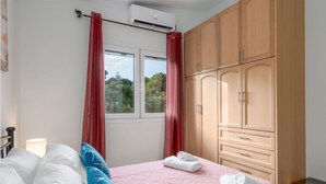 Quarto com cama, janela com cortinas vermelhas, guarda-roupa e luminária.