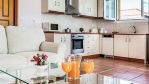 Eine moderne Küche mit weißen Schränken, einer Mikrowelle, einem Herd und einem Geschirrspüler. Ein Glastisch mit zwei Gläsern Orangensaft und einer Blumenschale.