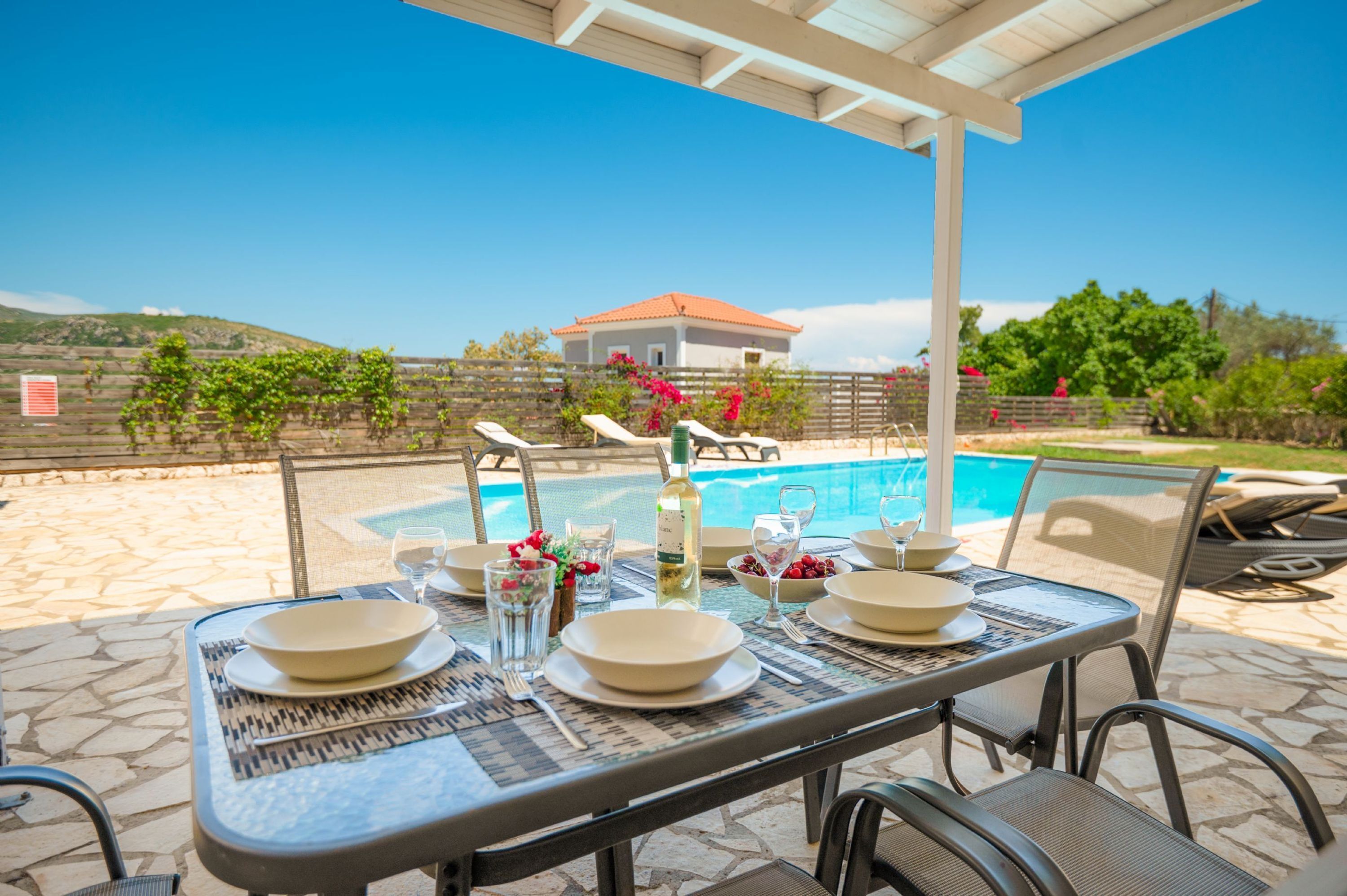 Une table dressée pour un repas, avec une piscine et une maison en arrière-plan.