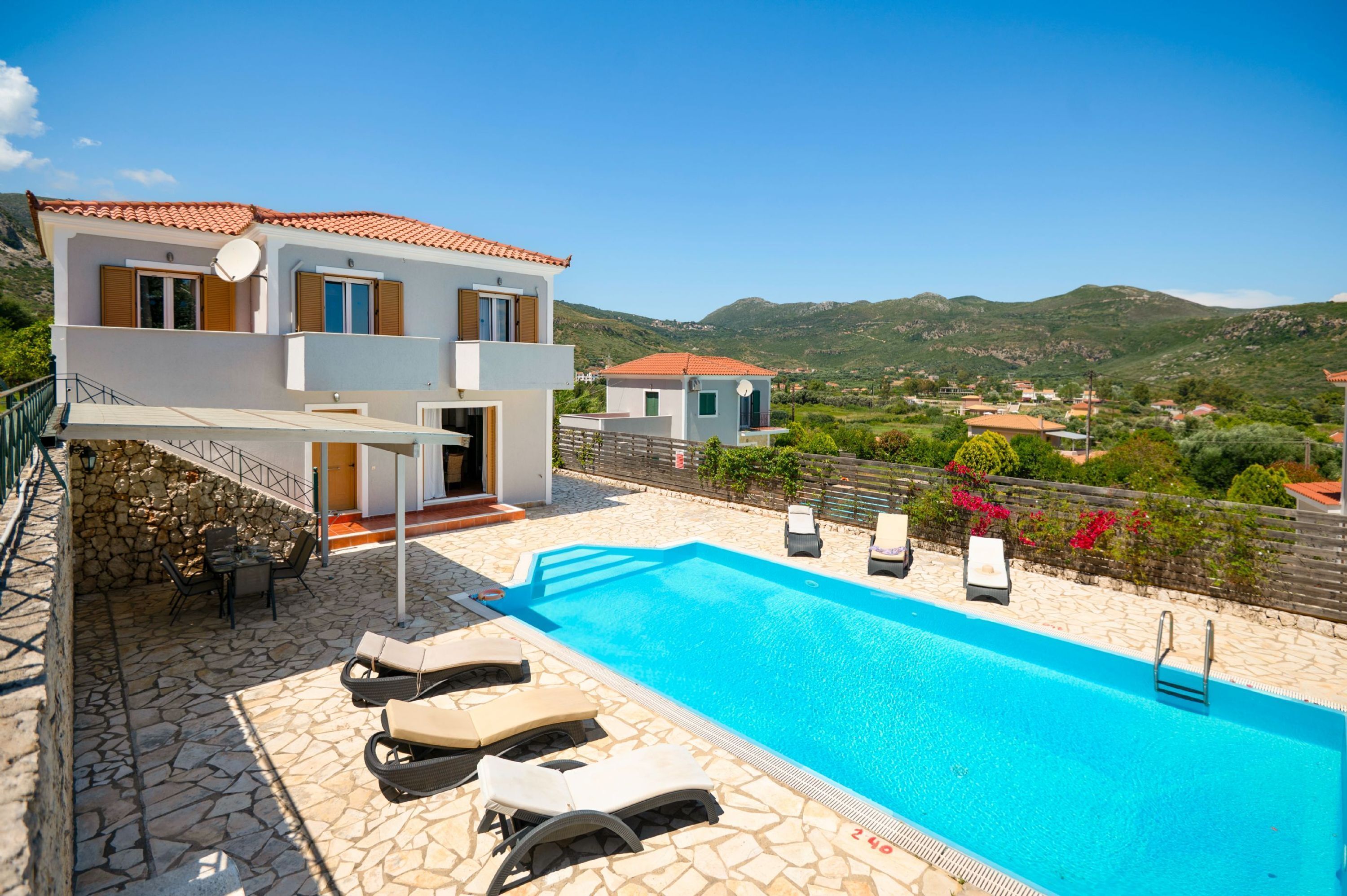 A modern two-story house with a swimming pool, stone patio, and a view of the surrounding hills.