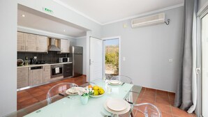 Een moderne keuken met een eetgedeelte, met een glazen tafel, uitzicht door de open deur en een ingebouwde airconditioning.