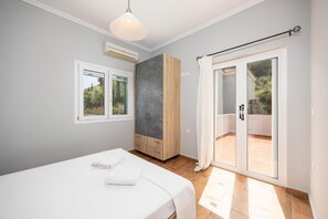 Ein Schlafzimmer mit Bett, Schrank, Fenster und einer Glastür zu einem Außenbereich.