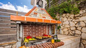Een buitenbarbecue van baksteen met een achtergrond van een stenen muur, met diverse gegrilde groenten en satés.