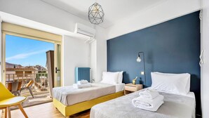 Hotellihuone, jossa on kaksi sänkyä, parveke, josta on näkymä, keltainen tuoli ja moderni riippuvalaisin.
