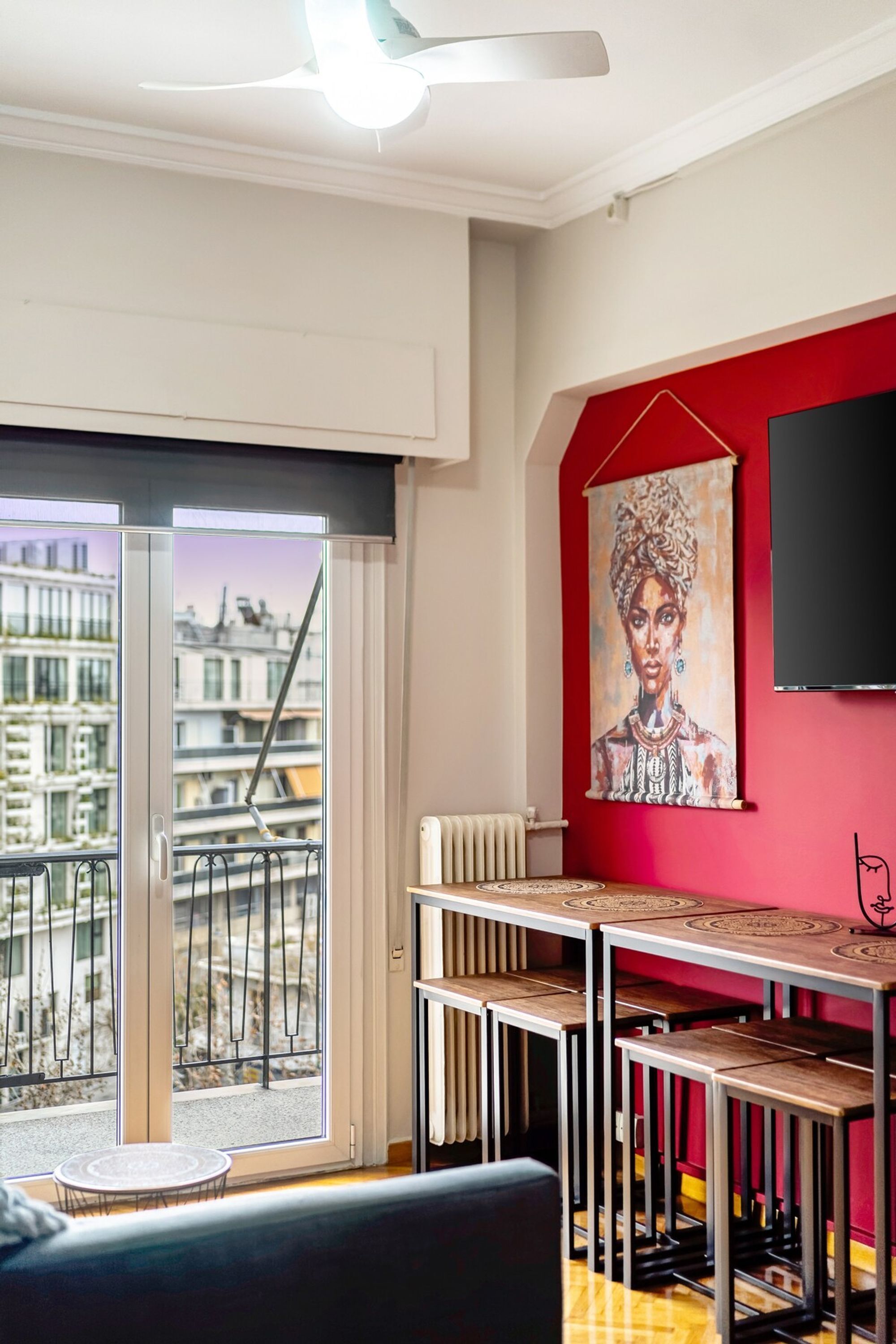 A modern living room with a large window, a red accent wall, and a painting.