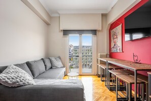 Ein modernes Wohnzimmer mit einem grauen Sofa, einem kleinen runden Tisch und einer Essecke mit Bänken.