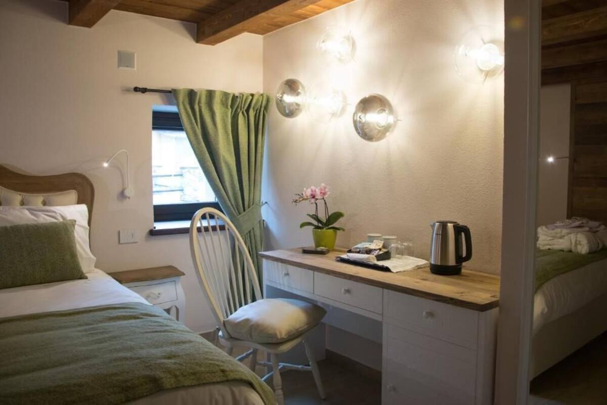 Un dormitorio con cama, escritorio y silla, ventana con cortinas, y lámpara de pared.