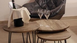 Un sillón de cuero oscuro, una mesa de centro de madera con dos copas de vino, y una botella de champán sobre una mesita.