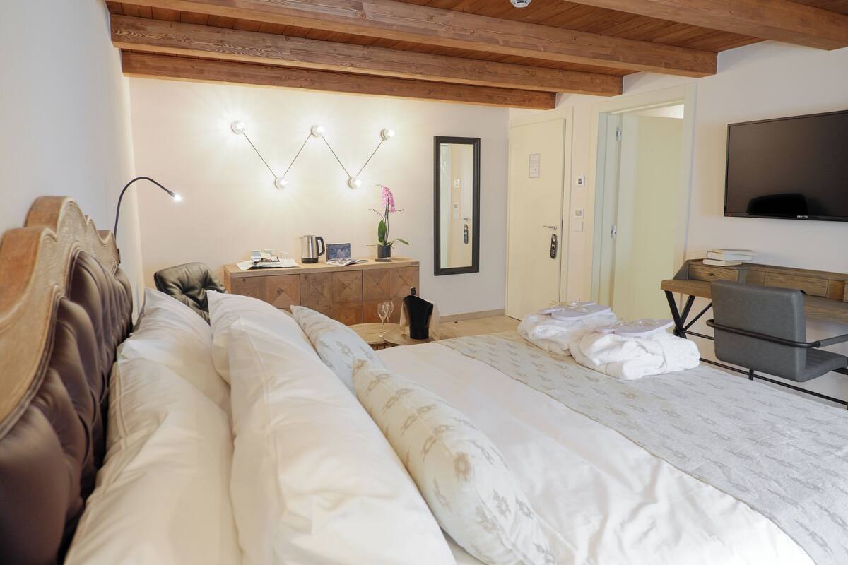 Un dormitorio con una cama grande, un cabecero de madera, una mesita de noche con lámpara, un aparador, un espejo y un televisor.