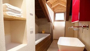 Un baño con una bañera independiente, un estante de madera con toallas y un armario rojo.