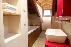 Un baño con una bañera independiente, un estante de madera con toallas y un armario rojo.