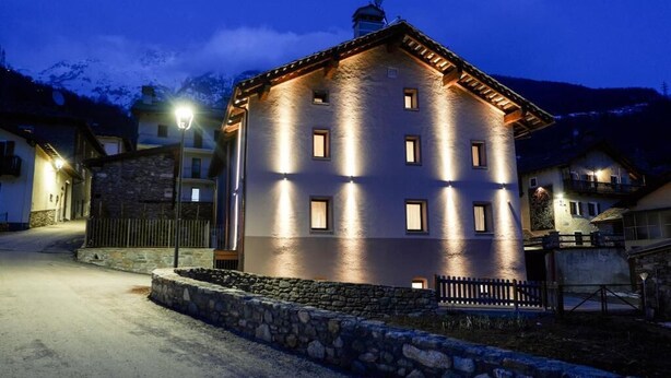 Un edificio de varios pisos con fachada de piedra y tejado inclinado, iluminado por luces exteriores.