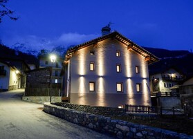 Un edificio de varios pisos con fachada de piedra y tejado inclinado, iluminado por luces exteriores.