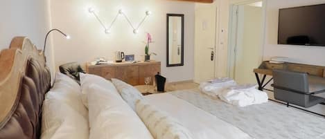 A bedroom with a large bed, wooden ceiling beams, a bedside table with a lamp, a mirror, and a TV mounted on the wall.