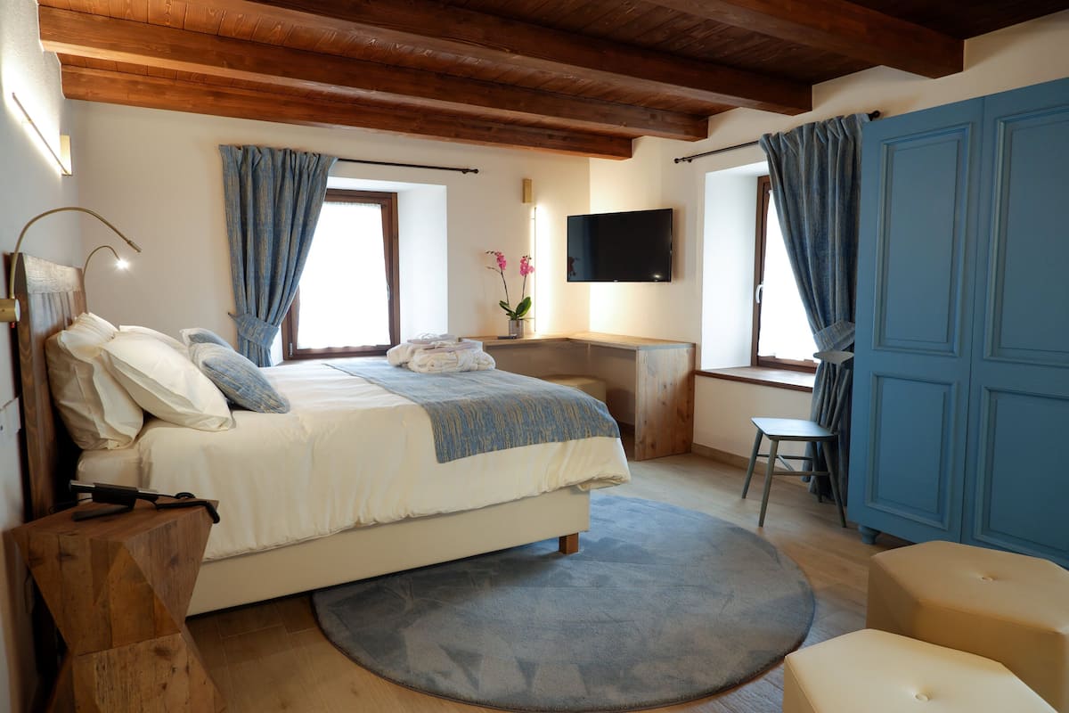 Un dormitorio con cama, escritorio, silla, televisión y vigas de madera.