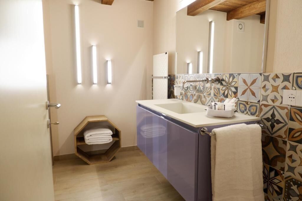 A bathroom with a sink, mirror, towel rack, and a shelf with folded towels.