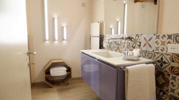 A bathroom with a sink, mirror, towel rack, and a shelf with folded towels.