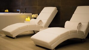 Dos sillones reclinables en un espacio de spa con bañera y velas.