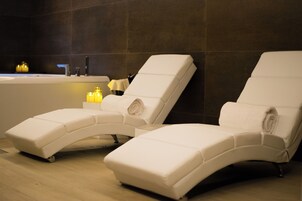 Dos sillones reclinables en un espacio de spa con bañera y velas.