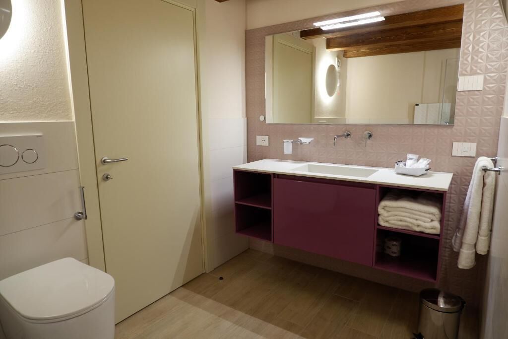 Een badkamer met een wit toilet, een wastafel met spiegel en een plank met handdoeken.