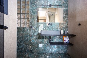 Un bagno con rivestimento in marmo, uno specchio, un lavandino e una doccia.