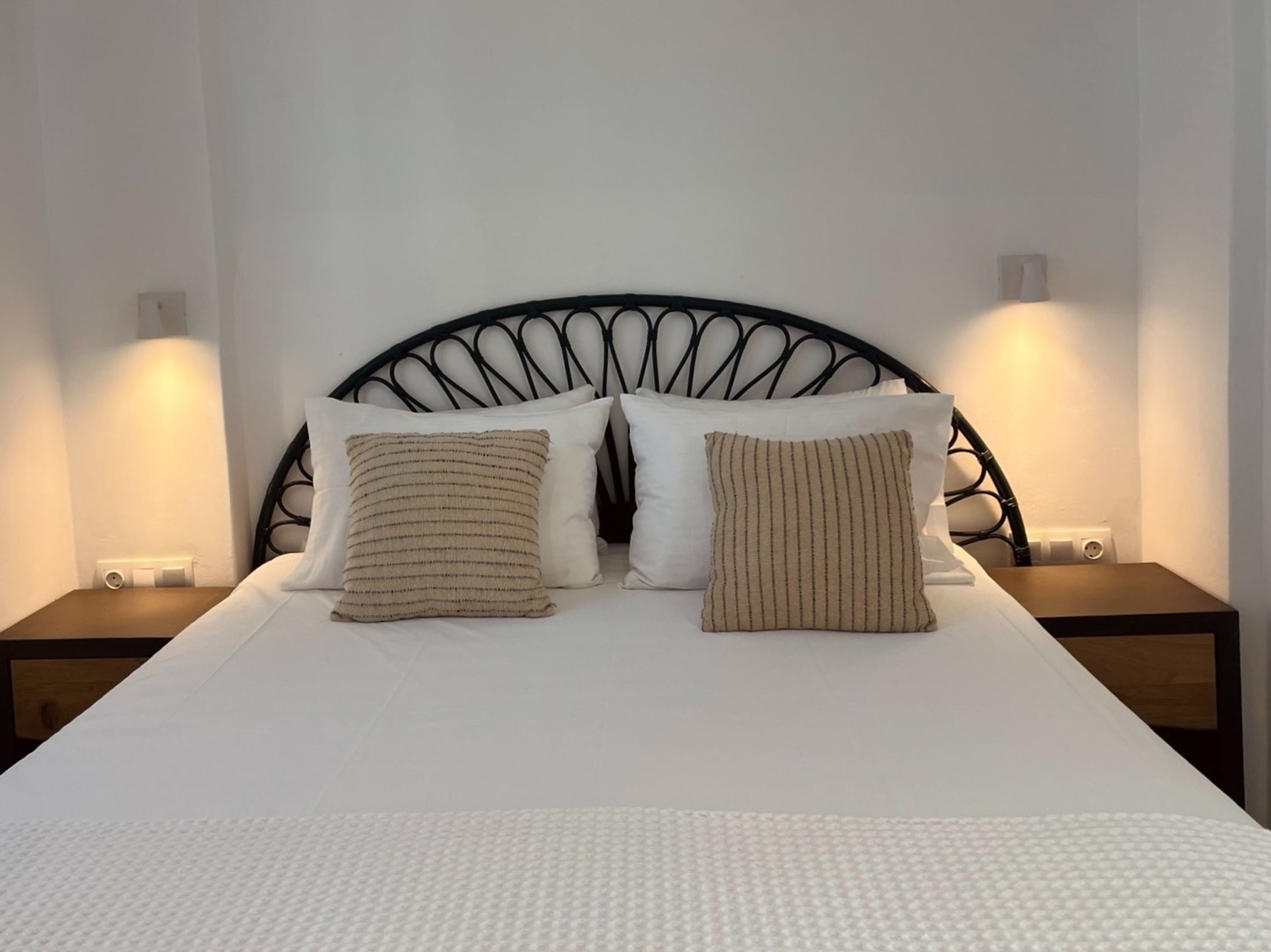 Een bed met een zwart metalen hoofdeinde, twee witte kussens en een bedspreide van witte stof met textuur.