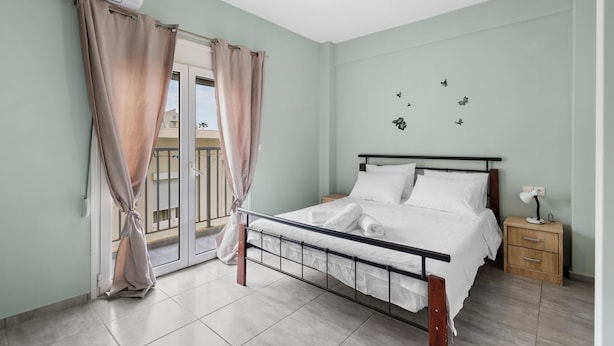 A bedroom with a bed, a nightstand, a window with curtains, and a wall with butterfly decorations. - Litsa’s Maisonette Near Sea - City Center (Chania)