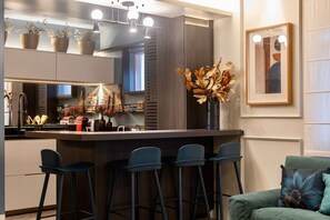 A modern kitchen with a bar area, bar stools, and a dining area with a sofa. - Flat no Jardins com Servi ço de Camareira (São Paulo)