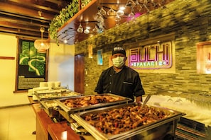 A buffet area with various food options, a chef, and a neon sign.