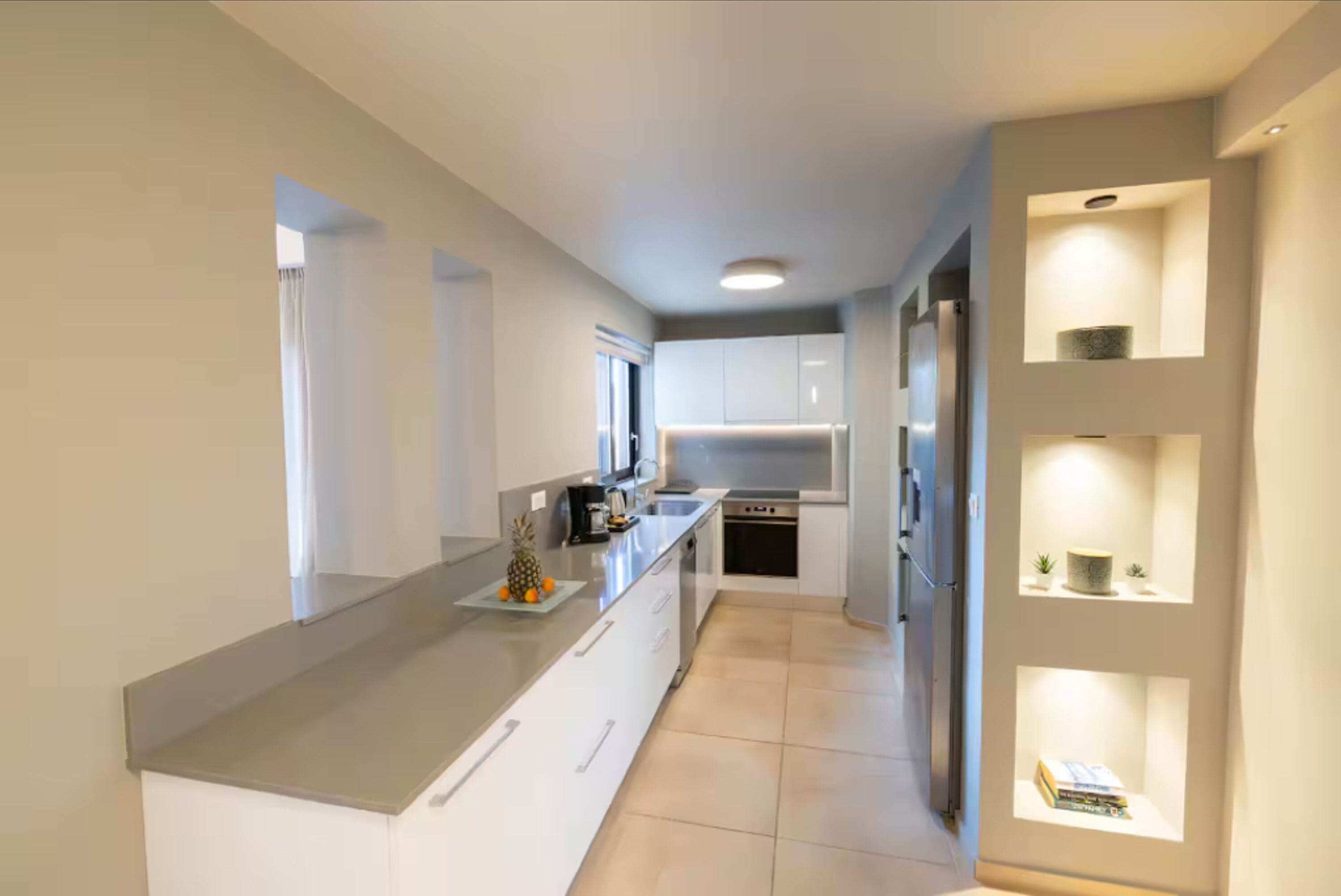 Una cocina moderna con armarios blancos, una isla grande y estanterías empotradas.