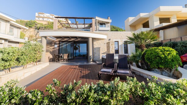 Een moderne villa met een houten terras, zitplaatsen buiten en uitzicht op omliggende gebouwen.