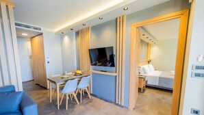 Een moderne hotelkamer met een zithoek, een tv aan de muur en een bed met een witte deken.