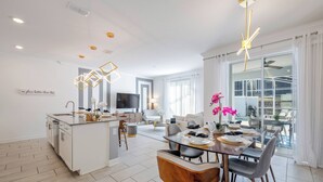 A modern kitchen with a central island, dining area with a table and chairs, and a living room with a sofa and TV. - CG1086 - 4BR house with pool near Disney area (Davenport)