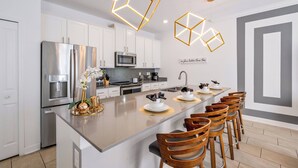 A modern kitchen with white cabinets, a stainless steel refrigerator, a microwave, and a large island with bar stools. - CG1086 - 4BR house with pool near Disney area (Davenport)