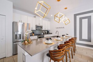 A modern kitchen with white cabinets, a stainless steel refrigerator, a microwave, and a large island with bar stools. - CG1086 - 4BR house with pool near Disney area (Davenport)