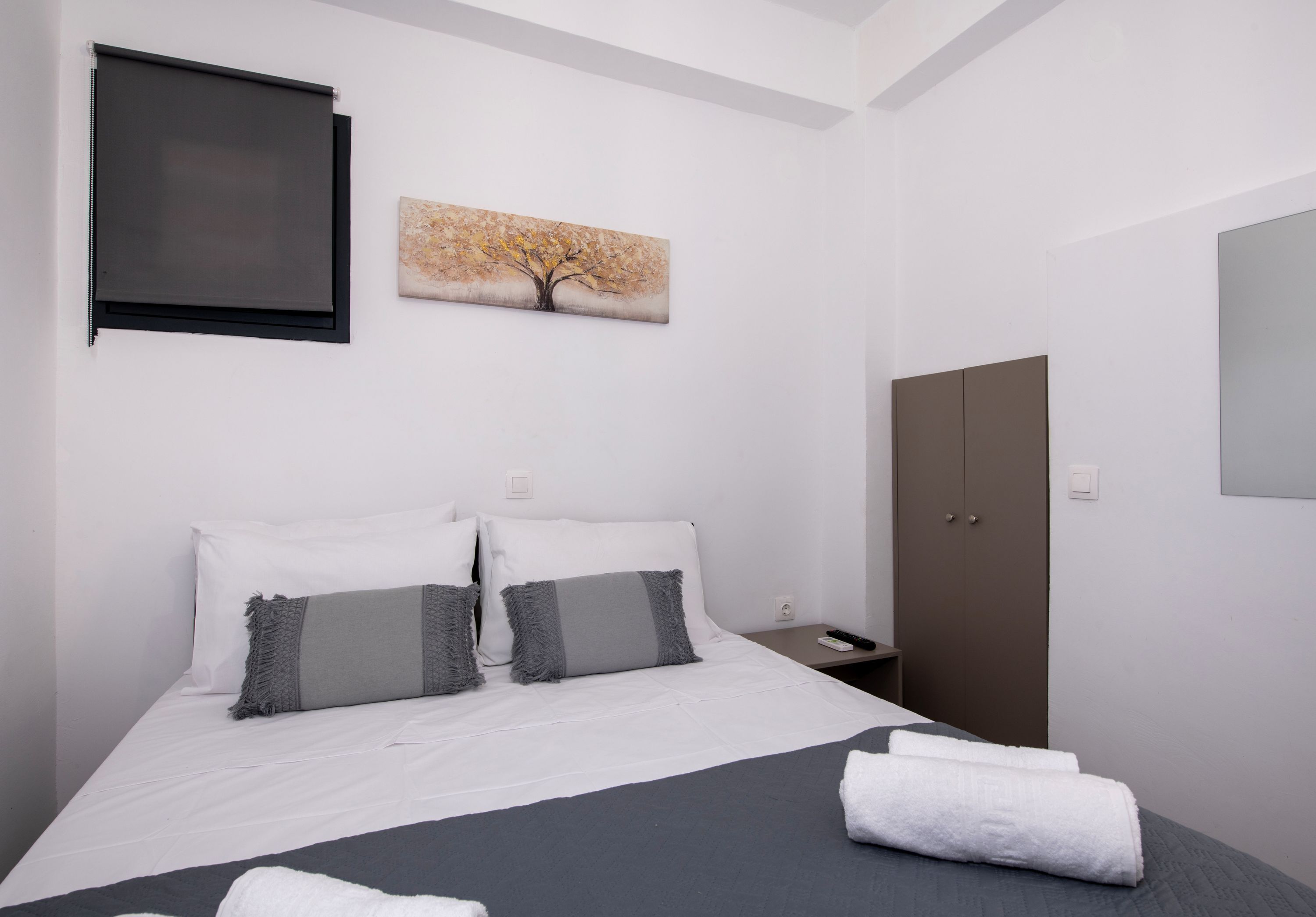 A bedroom with a bed, pillows, a painting, a wardrobe, and a bedside table.