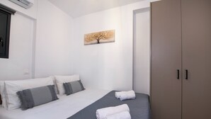 Uma cama bem arrumada com lençóis brancos, almofadas cinzas e um cobertor cinza, com duas toalhas enroladas sobre a cama.